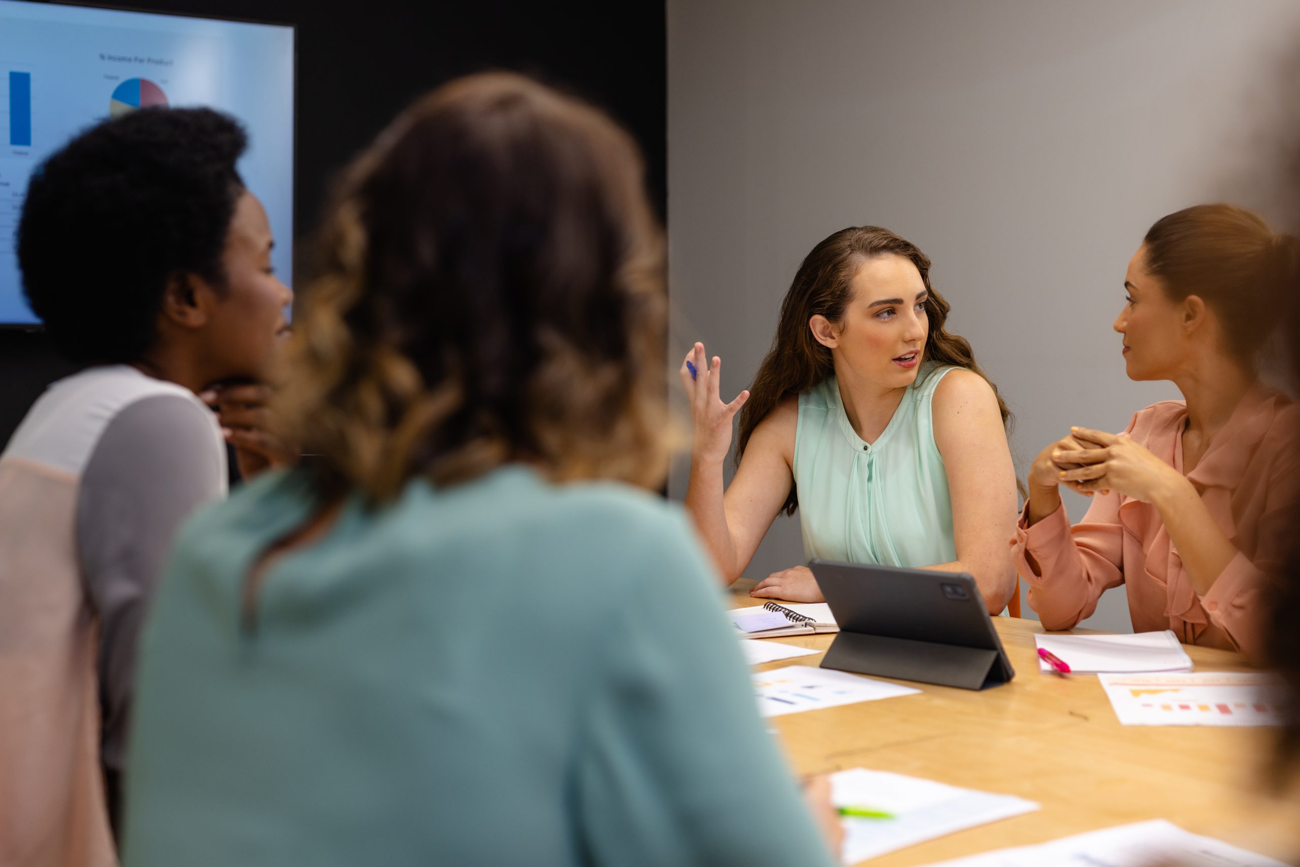 Diverse casual businesswomen in discussion using tablet in meeting room